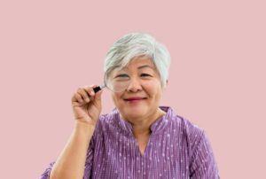 a middle aged asian woman smiles while holding up a magnifying glass